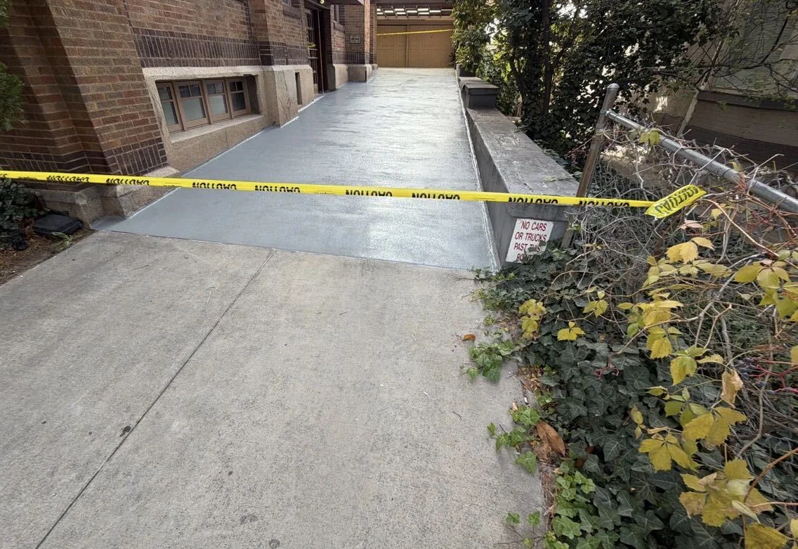 Gray coating on a concrete drive ramp beside a brick building